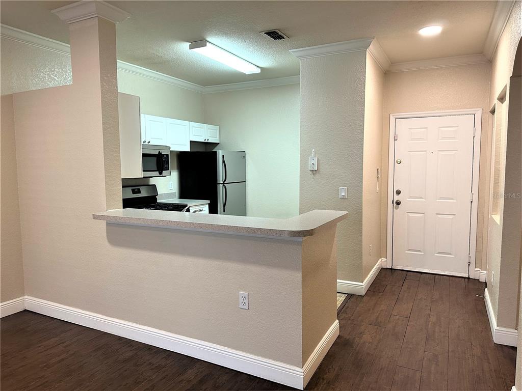 A kitchen with white cabinets and stainless appliances overlooks a living area with wood flooring — 3355 S KIRKMAN ROAD UNIT 1315, ORLANDO, FL