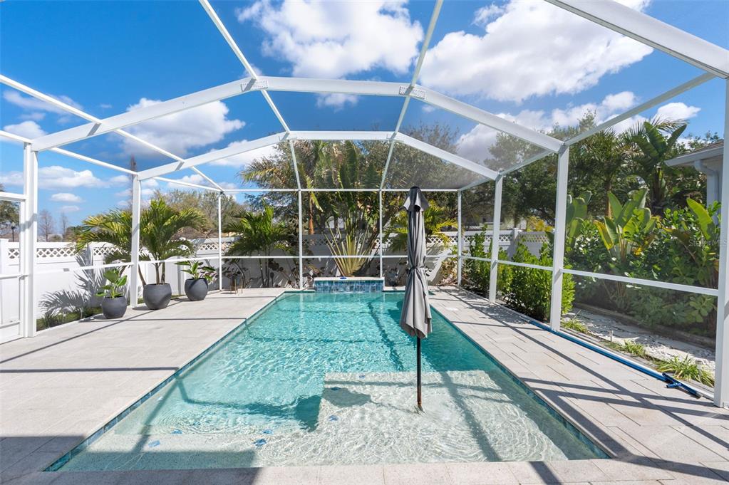 A swimming pool with a sun shelf and umbrella sits inside a screened-in patio enclosure — 325 SHORE CRAB WAY, APOLLO BEACH, FL