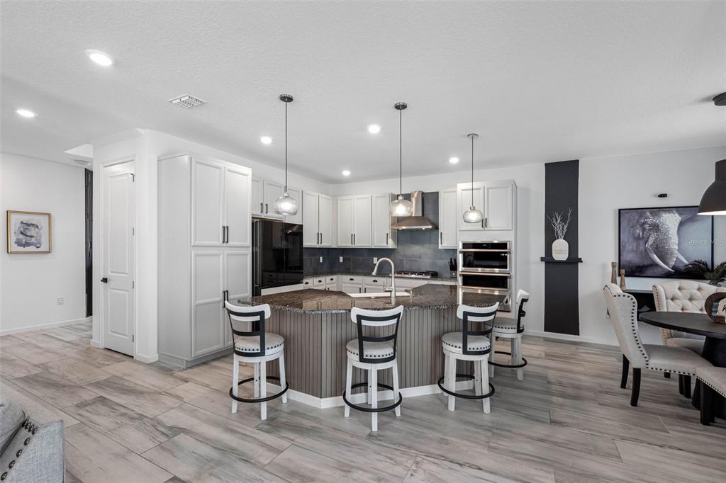 A kitchen features white cabinetry, a dark granite island with bar seating, and wood-look flooring — 325 SHORE CRAB WAY, APOLLO BEACH, FL