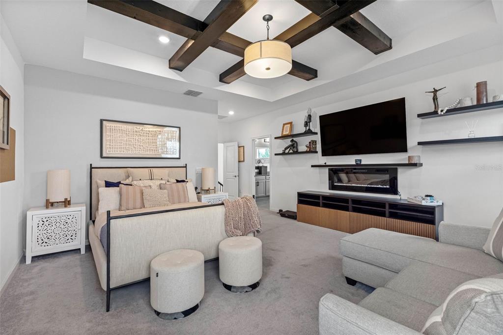 A bedroom features a tray ceiling with dark wood beams, a fireplace, and a television — 325 SHORE CRAB WAY, APOLLO BEACH, FL