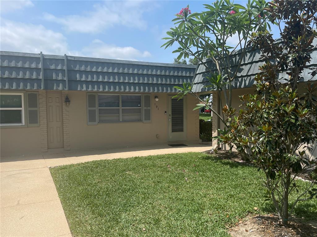 A single-story residential building exterior features a tan facade, gray mansard roof, and front lawn — 1802 BEDFORD TERRACE UNIT 191, SUN CITY CENTER, FL