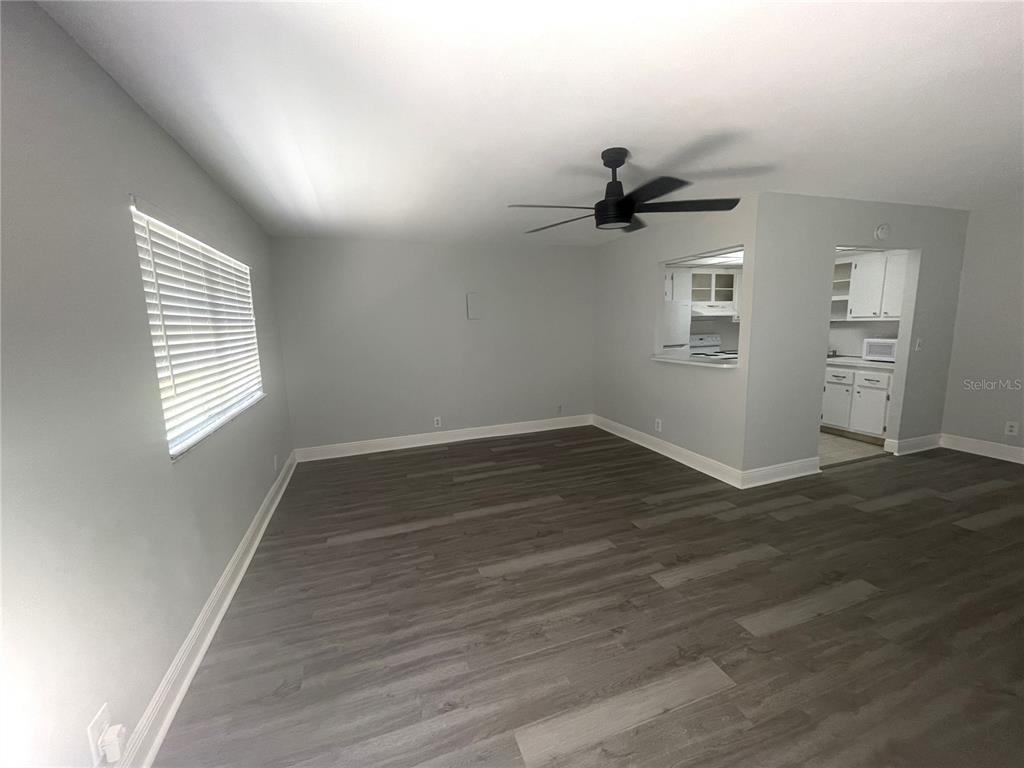 An empty living room with gray walls, wood-look flooring, a ceiling fan, and kitchen pass-through — 1802 BEDFORD TERRACE UNIT 191, SUN CITY CENTER, FL