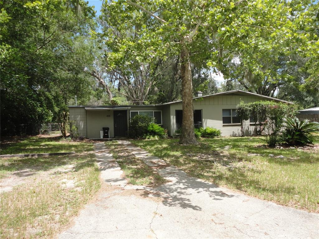 A single-story house with light green siding and a concrete driveway sits among mature trees — 401 NW 36TH TERRACE, GAINESVILLE, FL