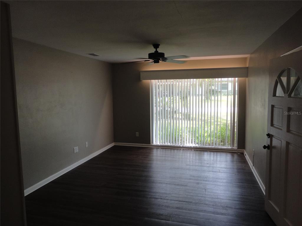 An empty living room features dark wood-look flooring, gray walls, and a large sliding glass door — 401 NW 36TH TERRACE, GAINESVILLE, FL