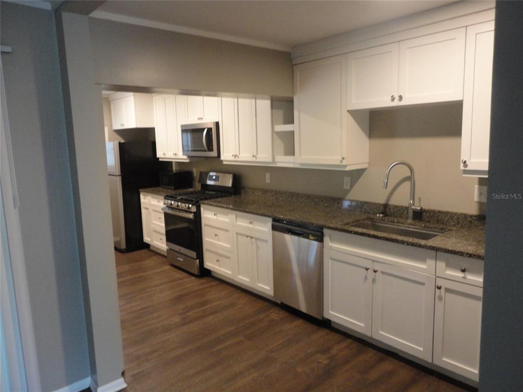 A kitchen features white cabinets, granite countertops, stainless steel appliances, and wood-look flooring — 401 NW 36TH TERRACE, GAINESVILLE, FL