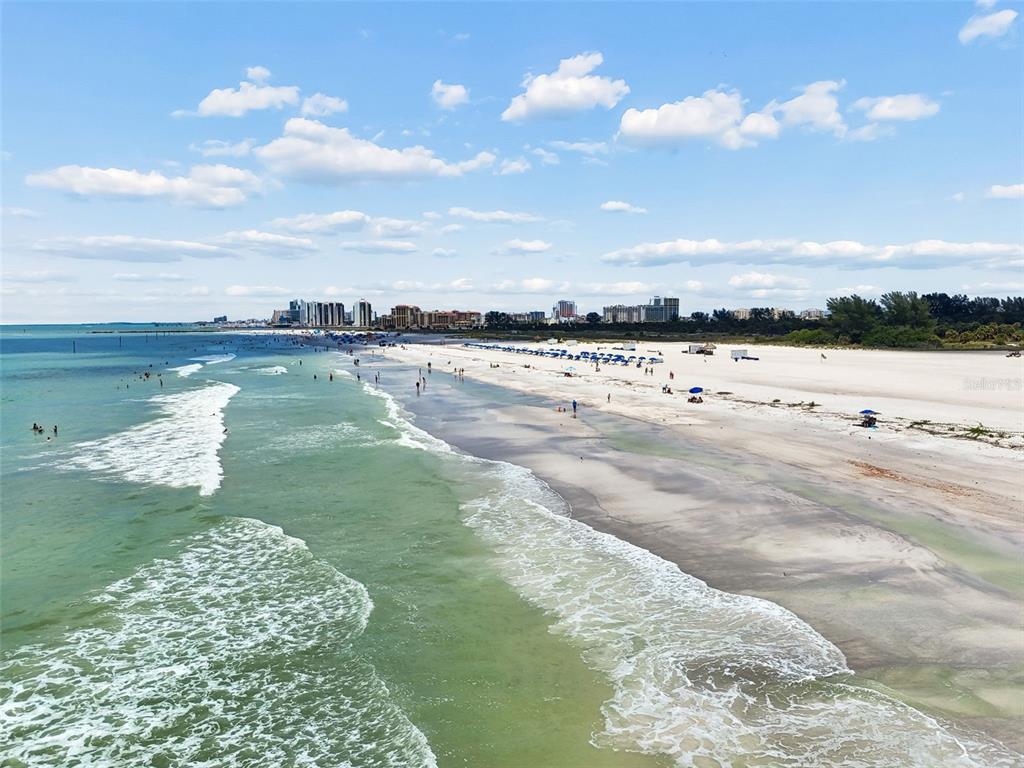 An aerial view of a sandy beach with ocean waves and distant high-rise buildings — 1170 GULF BOULEVARD UNIT 403, CLEARWATER BEACH, FL