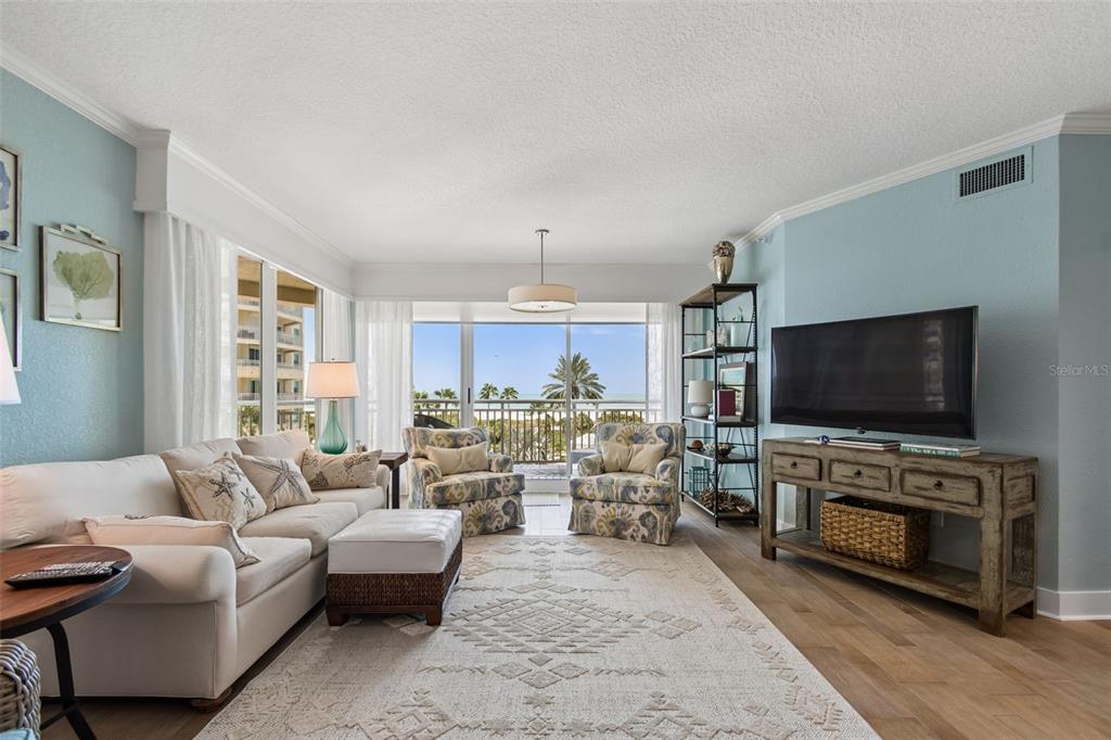 A living room features light blue walls, a white sofa, patterned armchairs, and a balcony view — 1170 GULF BOULEVARD UNIT 403, CLEARWATER BEACH, FL