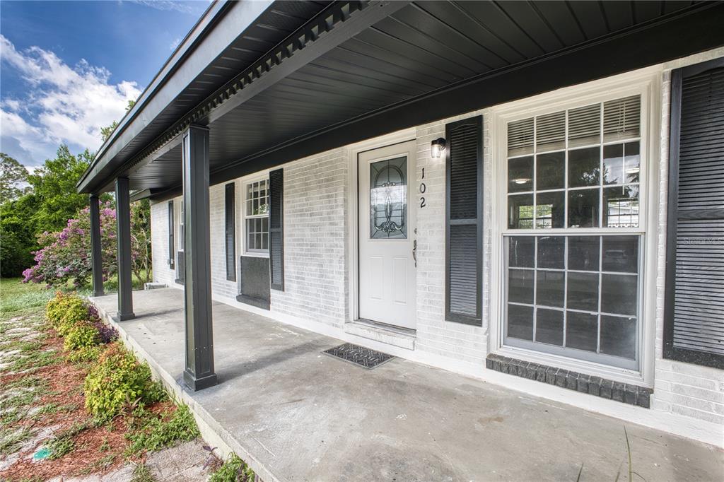 A white brick house exterior features a covered front porch with black columns and shutters — 102 AMIGOS ROAD, DEBARY, FL