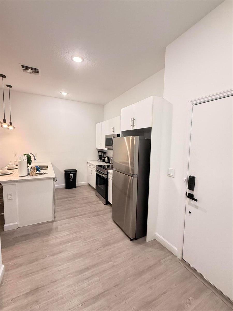 A modern kitchen features white cabinetry, stainless steel appliances, and light wood-look flooring — 653 Trikomo Drive, Davenport FL 33896, DAVENPORT, FL