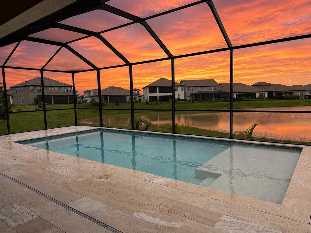 A screened-in swimming pool patio overlooks a pond and houses at sunset — 11105 RUSTIC TIMBER LOOP, SAN ANTONIO, FL