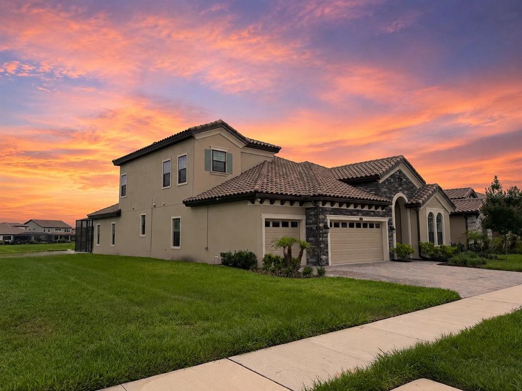 A two-story house with a stone facade, tile roof, and attached garage at sunset — 11105 RUSTIC TIMBER LOOP, SAN ANTONIO, FL