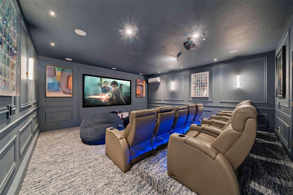 A home theater room features tiered rows of leather seating, a projector screen, and blue lighting — 9127 TURQUOISE WAVE COVE, KISSIMMEE, FL