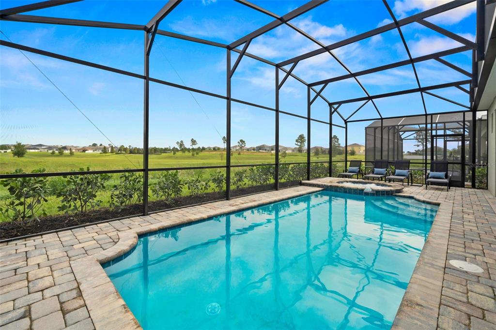 A screened-in pool and spa area with a brick paver deck overlooking a grassy field — 9127 TURQUOISE WAVE COVE, KISSIMMEE, FL