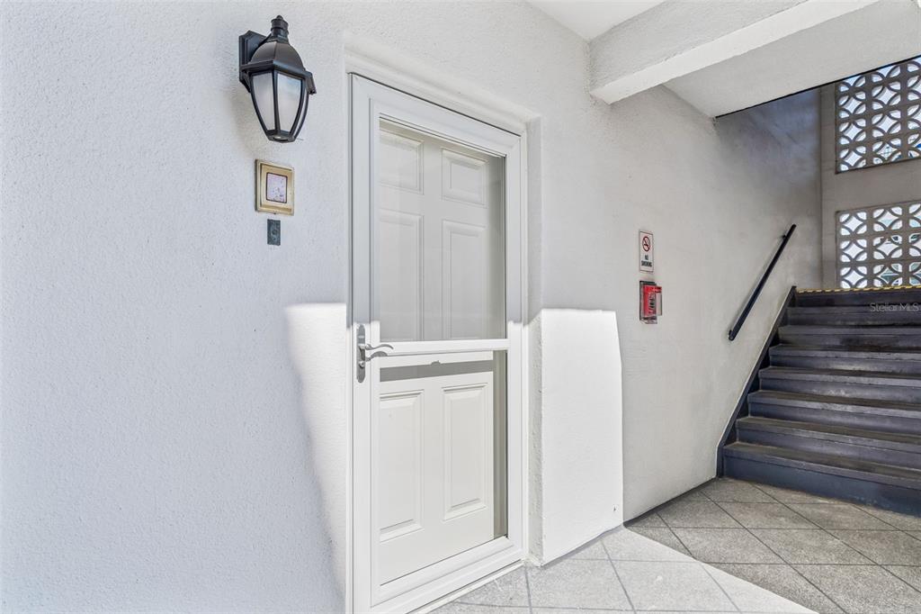 A white door with a storm door sits next to a staircase and outdoor lighting — 5960 30TH AVENUE S UNIT 114, GULFPORT, FL