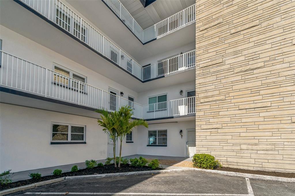 An exterior view of a multi-story apartment building with white walls and stone siding — 5960 30TH AVENUE S UNIT 114, GULFPORT, FL