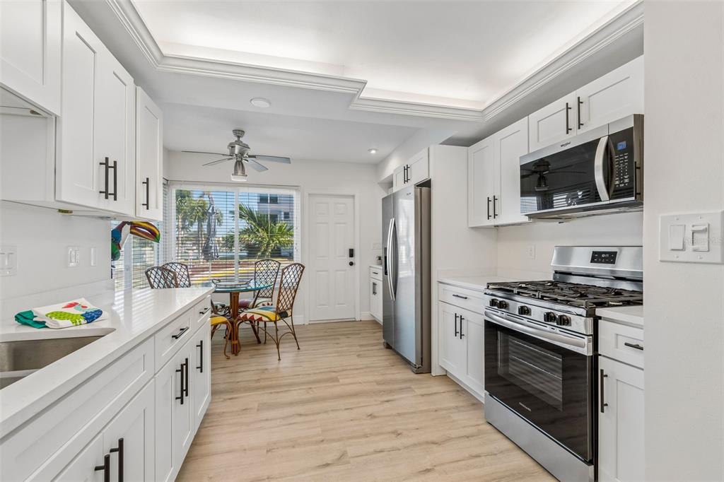 A bright kitchen features white cabinets, stainless steel appliances, quartz countertops, and a dining area — 5960 30TH AVENUE S UNIT 114, GULFPORT, FL