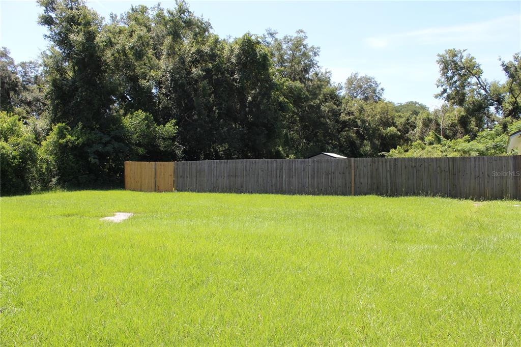 A grassy, vacant lot features a wooden privacy fence and dense trees in the background — 11413 PRUETT ROAD, SEFFNER, FL