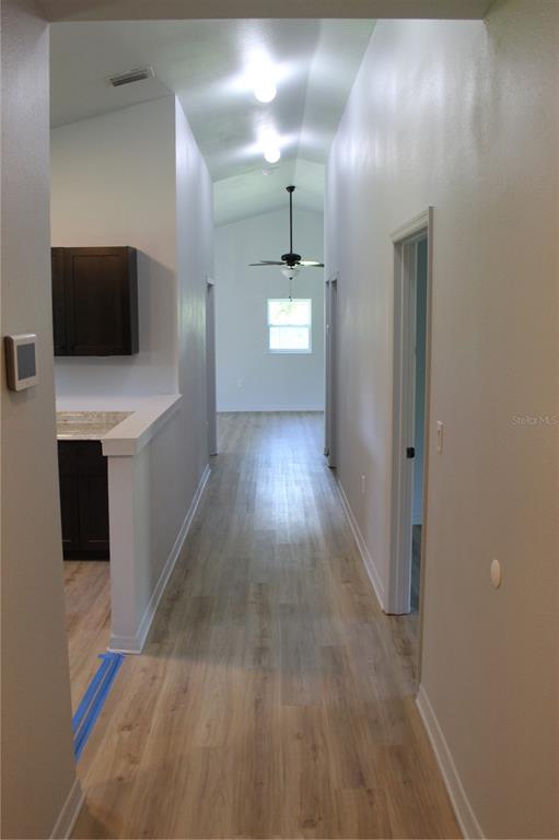 A hallway with light wood-look flooring leads toward a room with a ceiling fan — 11413 PRUETT ROAD, SEFFNER, FL
