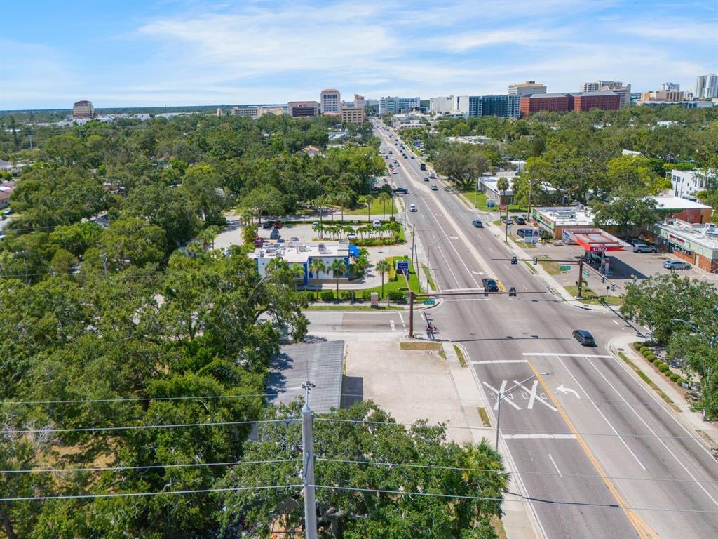 An aerial view shows a multi-lane road intersection with surrounding trees, businesses, and distant buildings — 1000 N WASHINGTON BOULEVARD, SARASOTA, FL