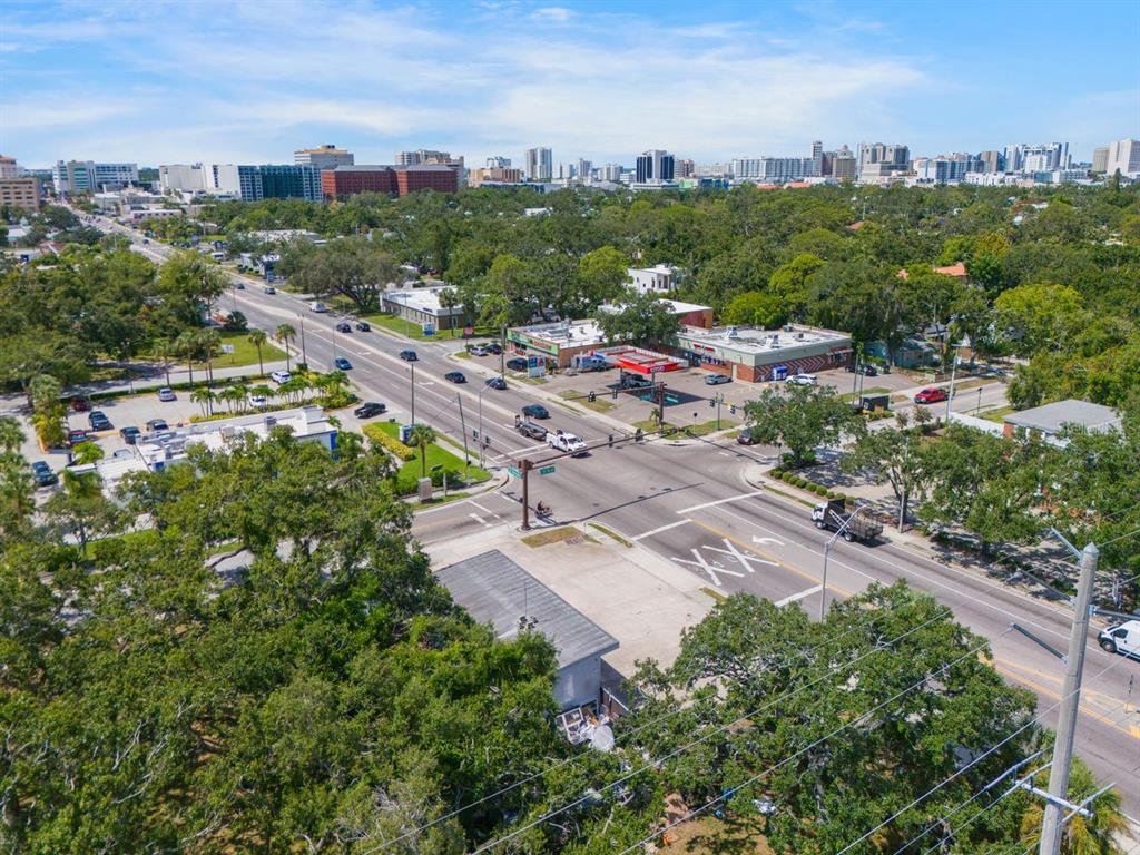 An aerial view of a street intersection surrounded by trees, commercial buildings, and a city skyline — 1000 N WASHINGTON BOULEVARD, SARASOTA, FL