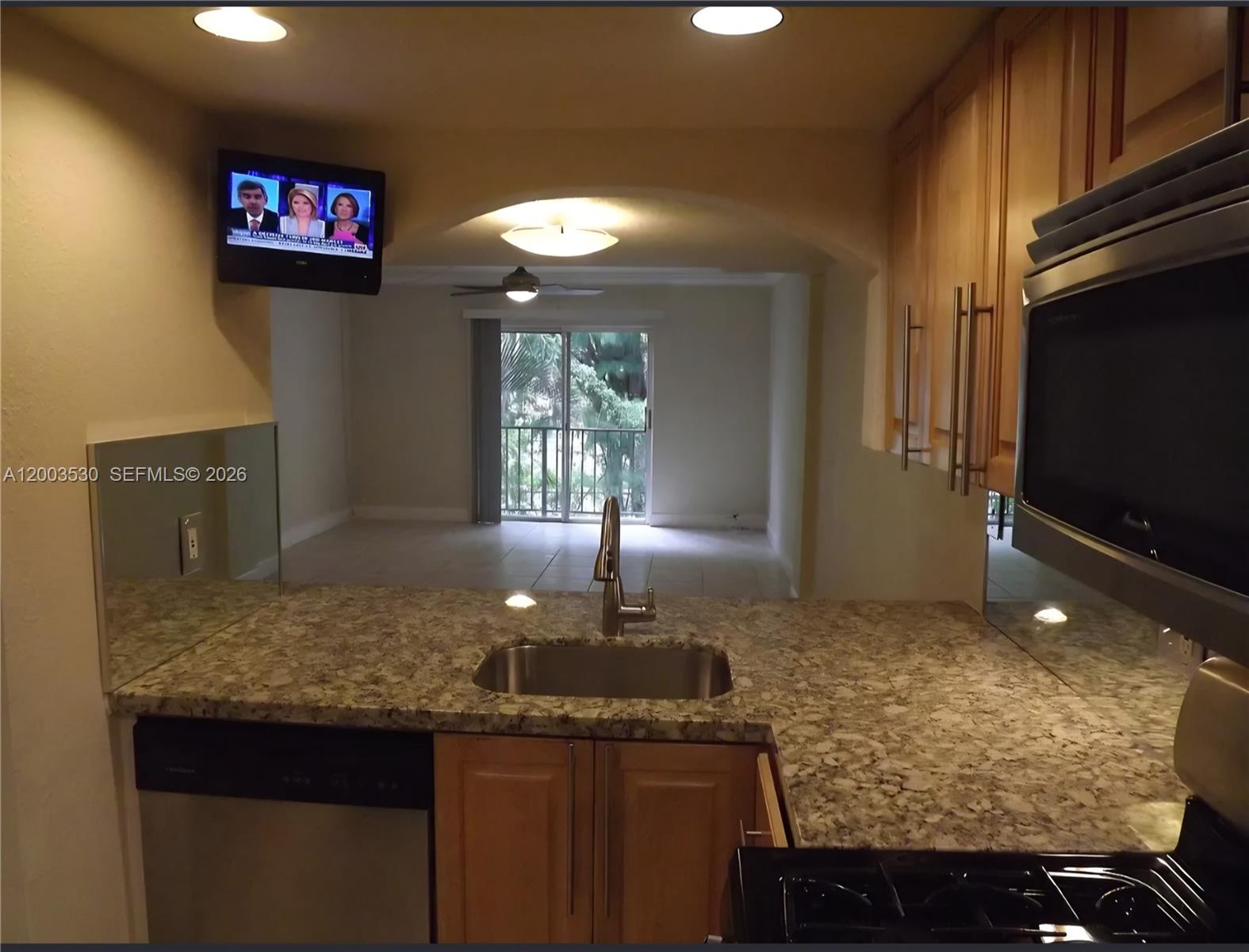 A kitchen with granite countertops and stainless steel appliances overlooks a living area with balcony — 6709 N Kendall Dr # 228, Pinecrest FL 33156, PINECREST, FL