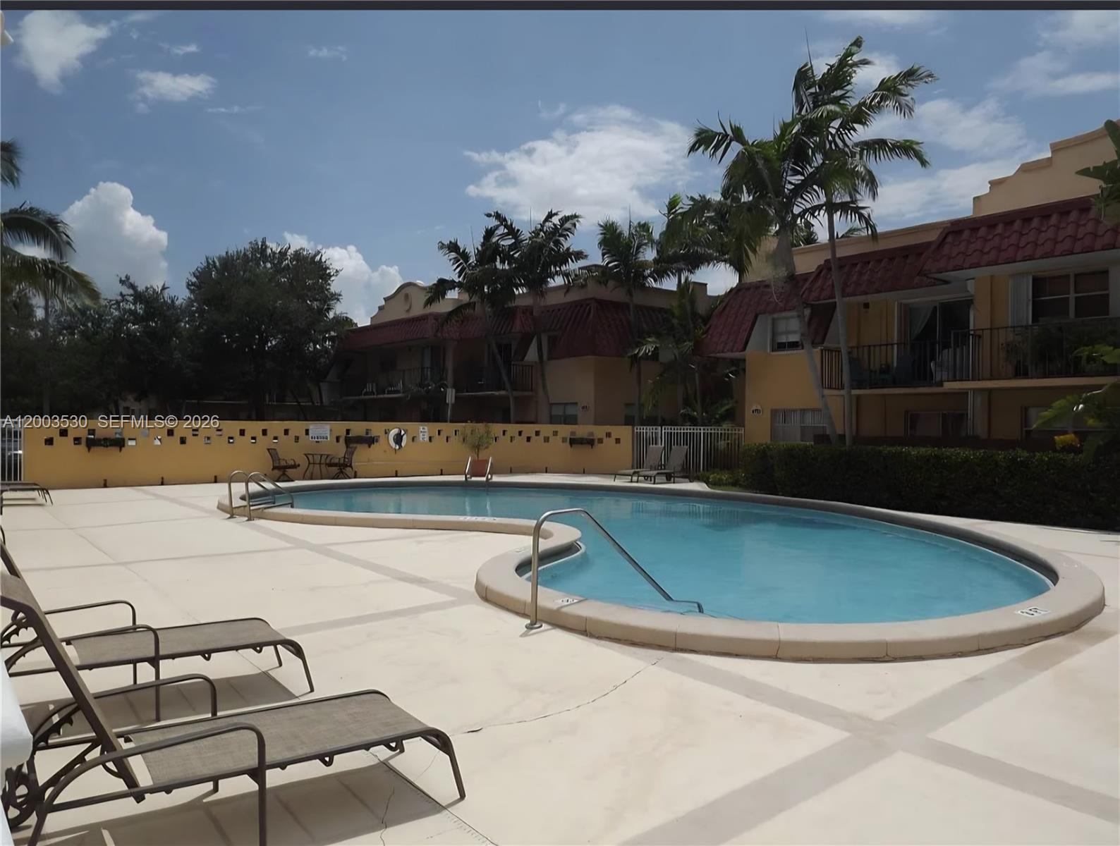 A kidney-shaped swimming pool sits on a concrete deck in front of apartment buildings — 6709 N Kendall Dr # 228, Pinecrest FL 33156, PINECREST, FL