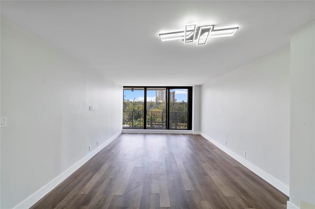 An empty room with white walls, dark wood-look flooring, a modern light fixture, and balcony access — 300 Three Islands Boulevard # 306, Hallandale Beach FL 33009, HALLANDALE BEACH, FL