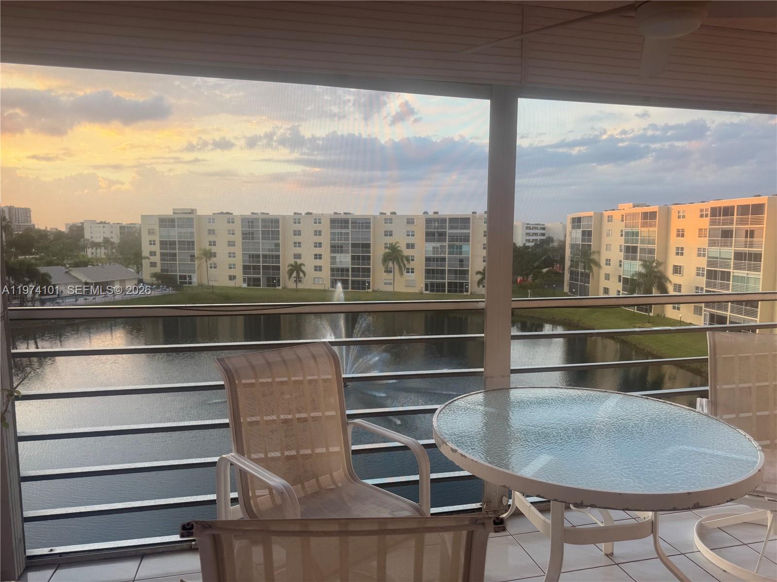 A balcony with patio furniture overlooks a lake, a fountain, and apartment buildings at sunset — 441 SE 3rd St # 505, Dania Beach FL 33004, DANIA BEACH, FL