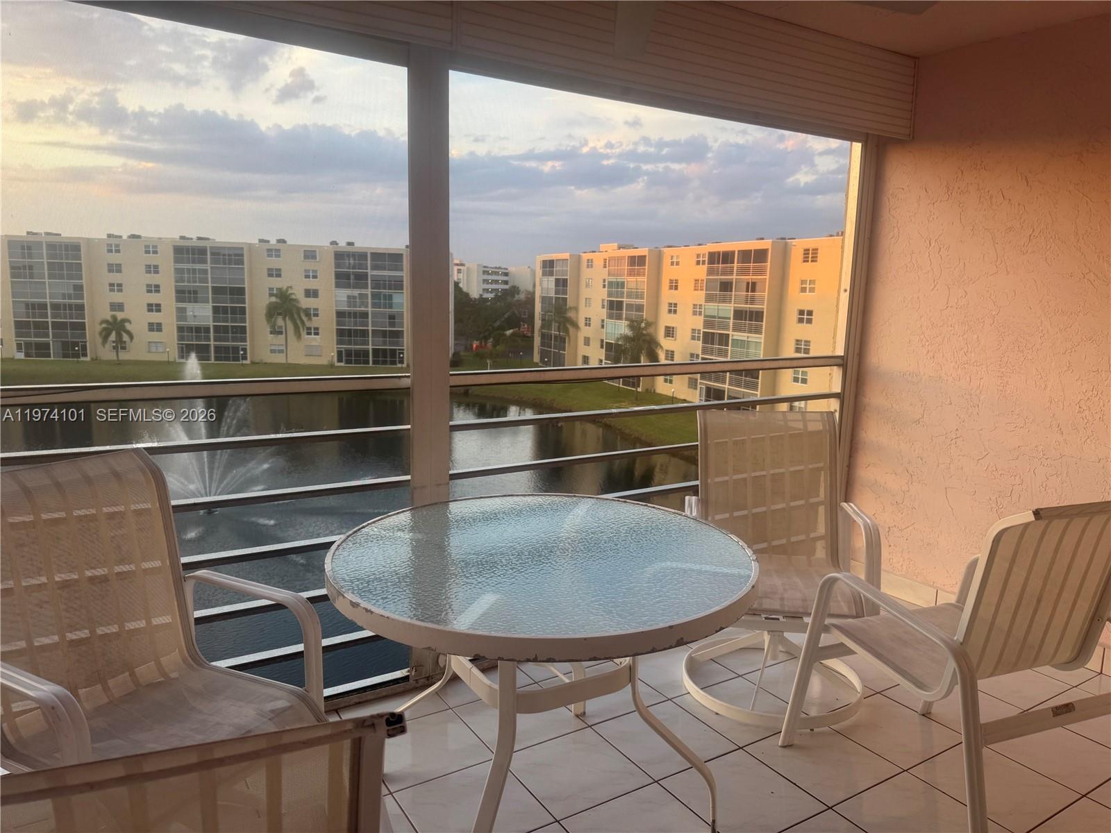 A screened-in balcony features a glass-top table, three chairs, and a view of a pond — 441 SE 3rd St # 505, Dania Beach FL 33004, DANIA BEACH, FL