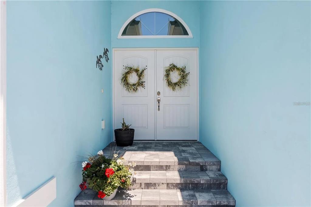 A light blue exterior wall frames a double front door with wreaths and stone steps — 10391 COQUINA COURT, PLACIDA, FL