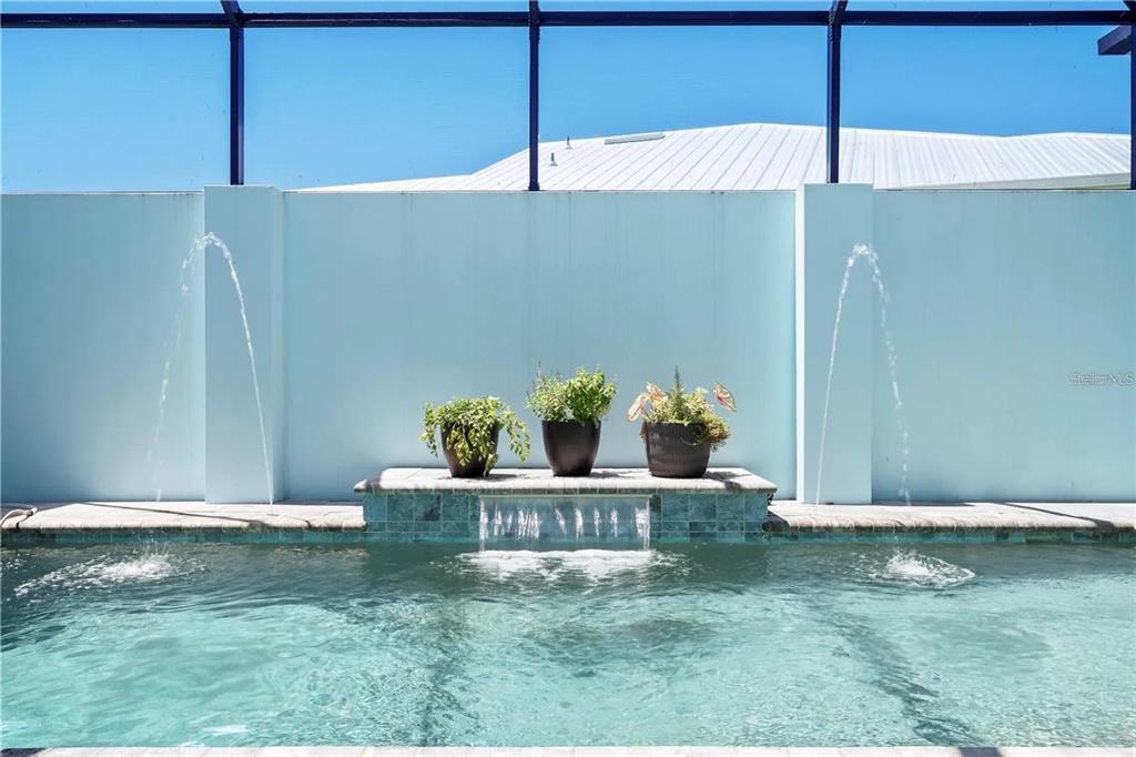 A swimming pool with a water feature, fountain jets, and three potted plants on a ledge — 10391 COQUINA COURT, PLACIDA, FL
