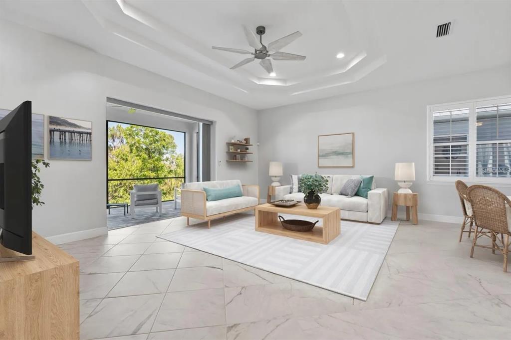 A bright living room features a tray ceiling, tile flooring, and a sliding door to a balcony — 10391 COQUINA COURT, PLACIDA, FL