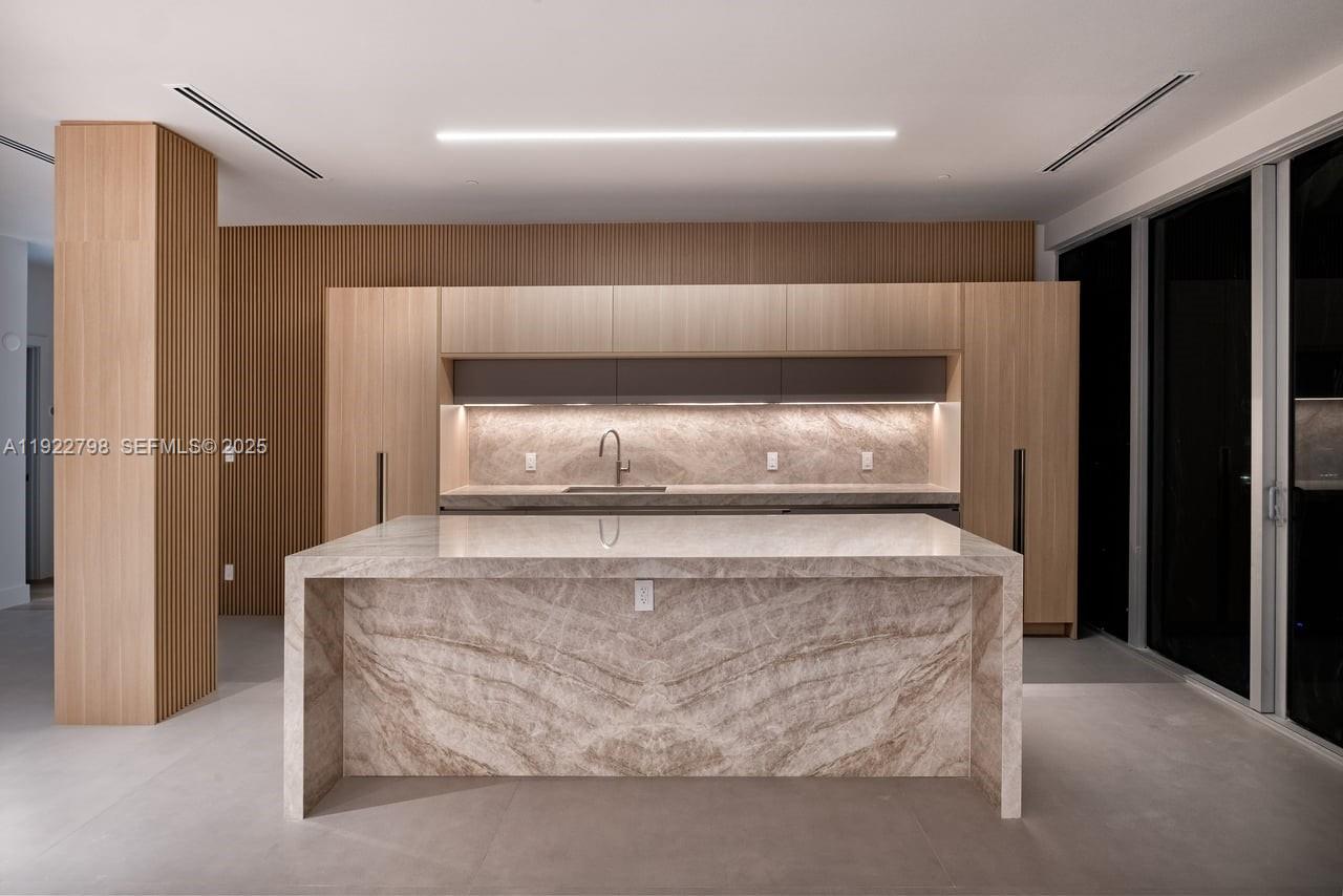A modern kitchen features a large marble waterfall island, light wood cabinetry, and slatted walls — 465 Brickell Ave # 5701, Miami FL 33131, MIAMI, FL