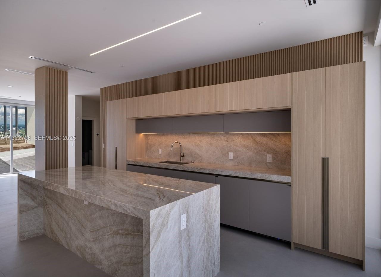 A modern kitchen features a stone waterfall island, light wood cabinetry, and gray lower cabinets — 465 Brickell Ave # 5701, Miami FL 33131, MIAMI, FL