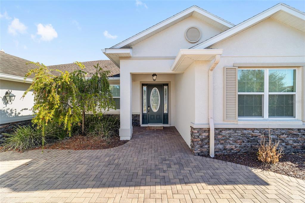 A paved walkway leads to the front entrance of a house with stone siding — 8889 SW 86TH LOOP, OCALA, FL