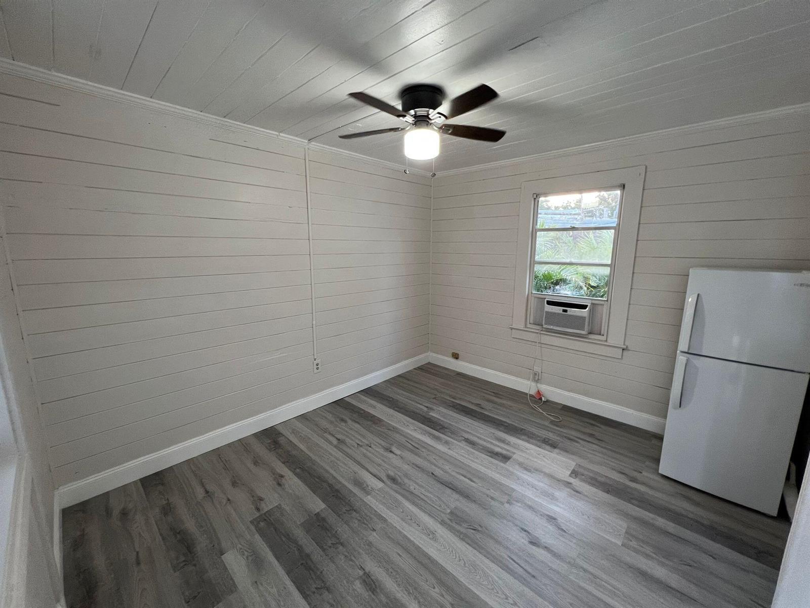 An empty room with light-colored shiplap walls, gray wood-look flooring, a ceiling fan, and refrigerator — 2843 Forest Hill Boulevard # 7, West Palm Beach FL 33406, WEST PALM BEACH, FL