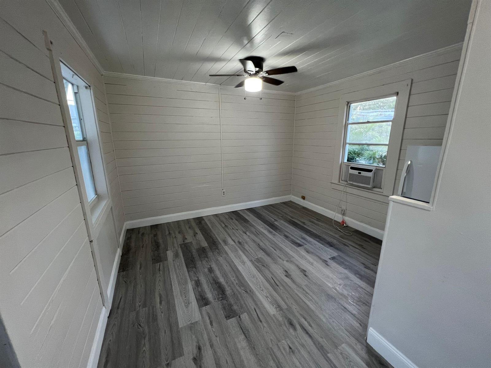 An empty room features light-colored horizontal wood walls, a ceiling fan, and gray wood-look flooring — 2843 Forest Hill Boulevard # 7, West Palm Beach FL 33406, WEST PALM BEACH, FL