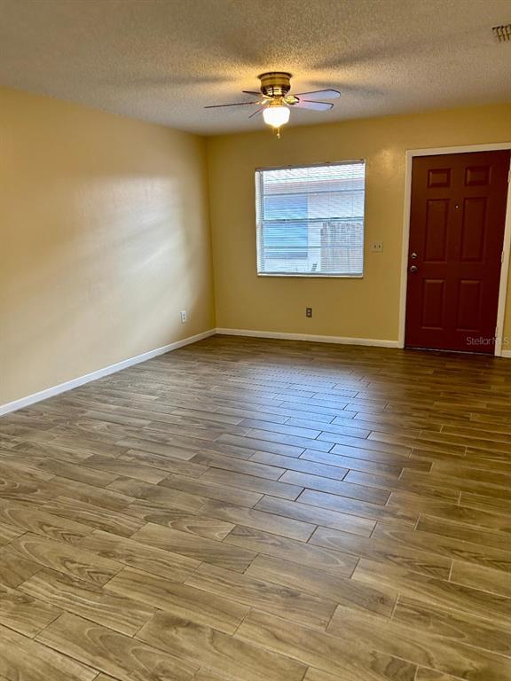 An empty room features light-colored walls, wood-look tile flooring, a ceiling fan, and a door — 8407 N 10TH STREET, TAMPA, FL