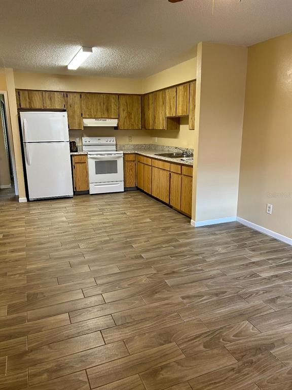 A kitchen features wood cabinets, white appliances, speckled countertops, and light wood-look tile flooring — 8407 N 10TH STREET, TAMPA, FL