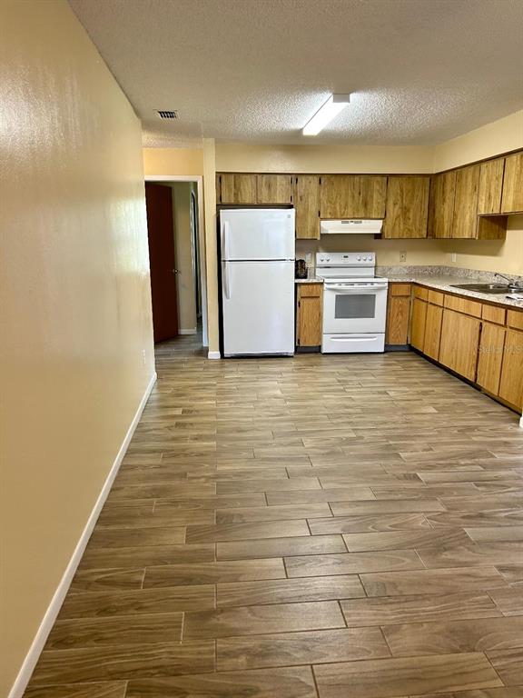 A kitchen features wood cabinets, white appliances, and light-colored wood-look tile flooring — 8407 N 10TH STREET, TAMPA, FL