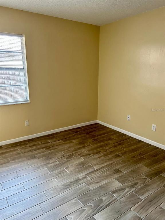 An empty room features light yellow walls, wood-look tile flooring, and a single window — 8407 N 10TH STREET, TAMPA, FL