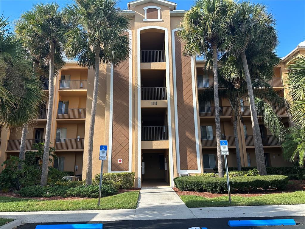 A multi-story apartment building exterior features tan stucco walls, brown diamond-patterned accents, and palm trees — 8105 GRAND ESTUARY TRAIL UNIT 404, BRADENTON, FL