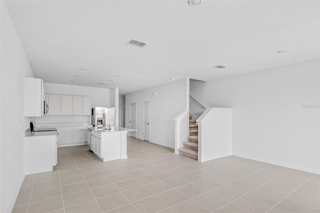 A bright, open-concept kitchen and living area featuring white cabinetry, tile flooring, and carpeted stairs — 391 SOL VISTA DRIVE, DUNDEE, FL