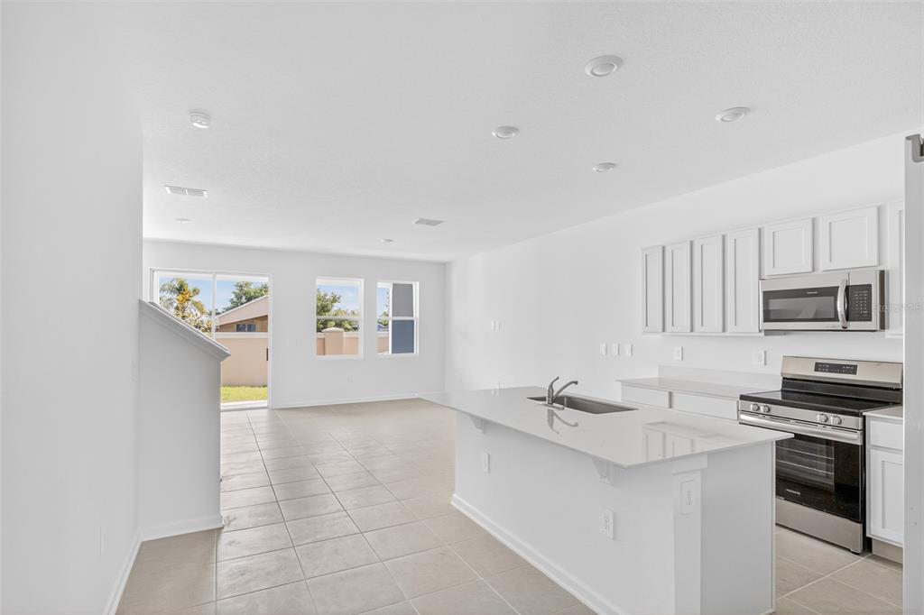 A bright kitchen with white cabinets, stainless steel appliances, and an island overlooks a living area — 391 SOL VISTA DRIVE, DUNDEE, FL