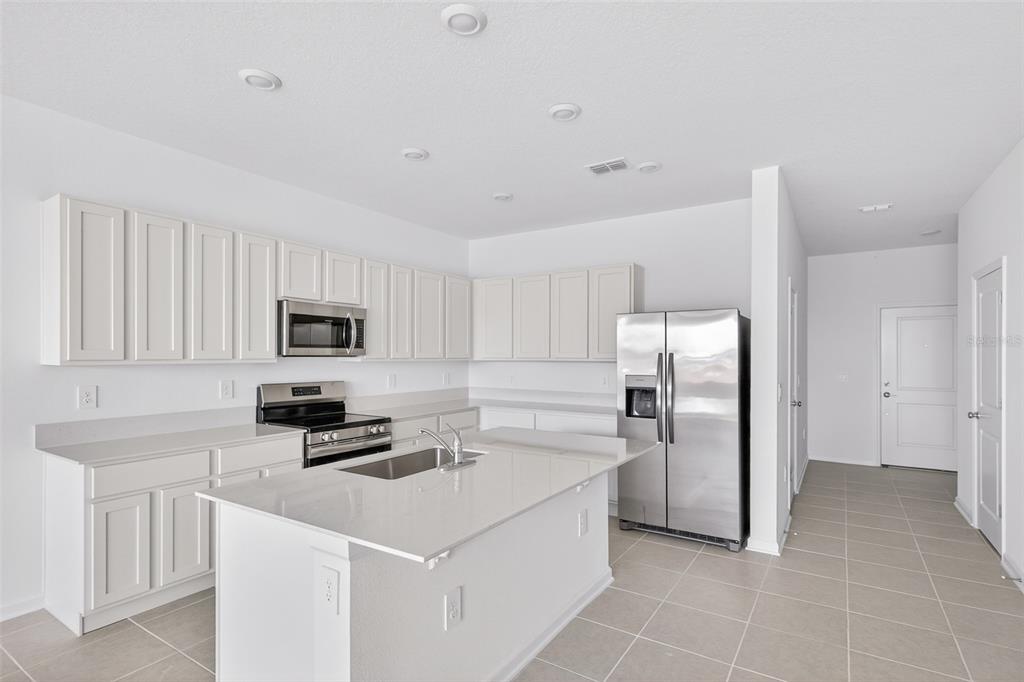 A modern kitchen features white cabinets, stainless steel appliances, a center island, and tile flooring — 391 SOL VISTA DRIVE, DUNDEE, FL