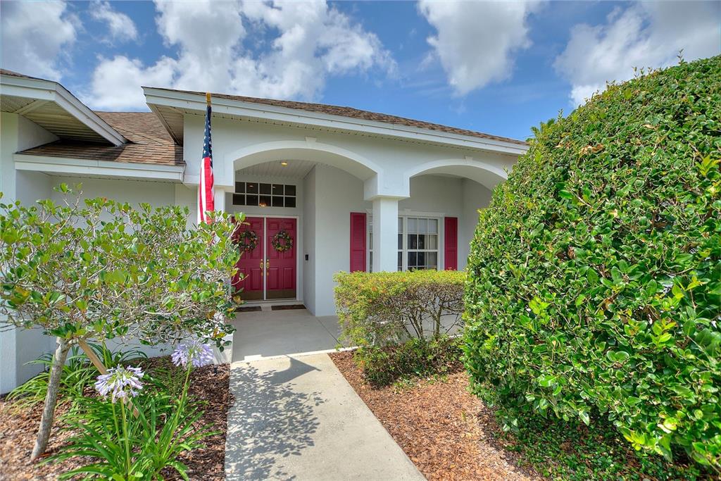 A white house exterior features a covered entryway with red double doors and shutters — 5521 EMERALD RIDGE BOULEVARD, LAKELAND, FL