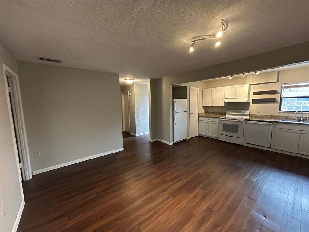 An open-concept living area features wood-look flooring and an adjacent kitchen with white cabinets — 2811 SW ARCHER ROAD UNIT C-18, GAINESVILLE, FL