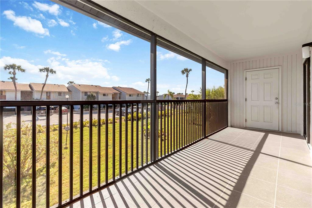 A covered balcony with tiled flooring, a black metal railing, and a white entry door — 5807 N ATLANTIC AVENUE UNIT 421, CAPE CANAVERAL, FL