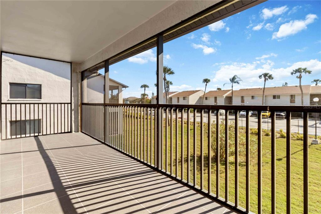 A covered balcony with tiled flooring and metal railings overlooks a parking lot and lawn — 5807 N ATLANTIC AVENUE UNIT 421, CAPE CANAVERAL, FL