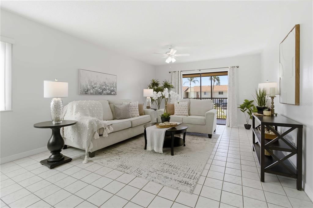 A bright living room features white tile floors, two beige sofas, and a sliding glass door — 5807 N ATLANTIC AVENUE UNIT 421, CAPE CANAVERAL, FL